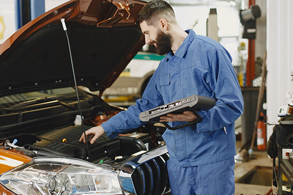 Young Caucasian Mechanic working under the hood of a car inside a garage.